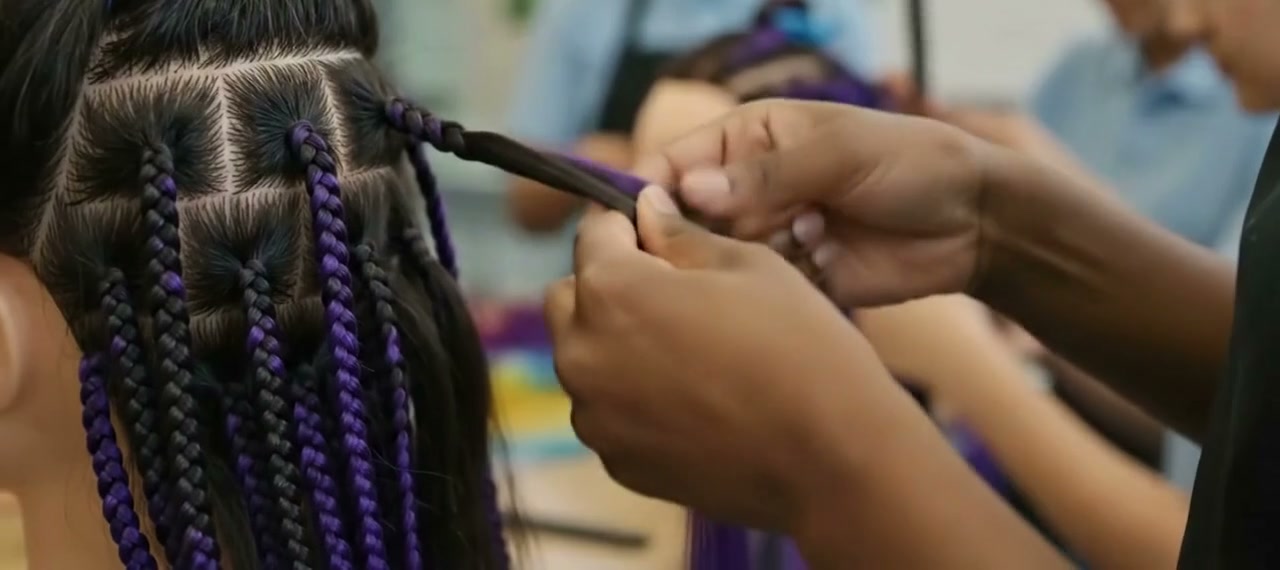 Close-up of hands braiding purple extensions into a participant’s hair at a workshop