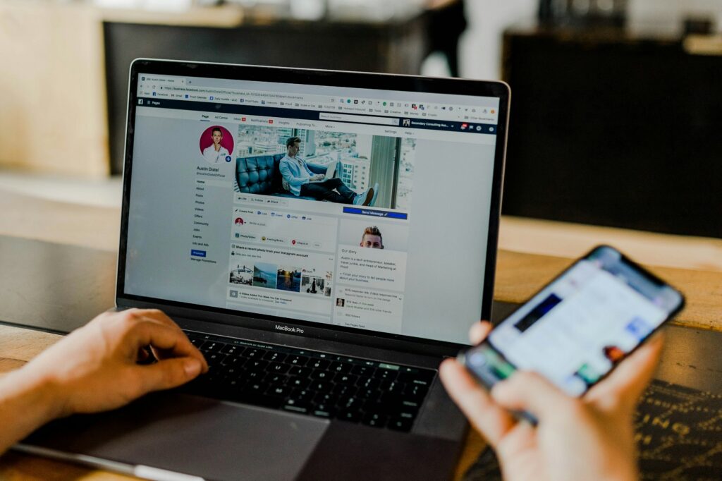 A person viewing a business Facebook page on both a laptop and a smartphone at the same time.