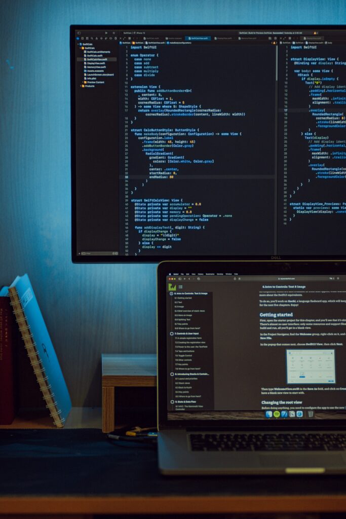 A laptop and external monitor on a desk displaying lines of programming code